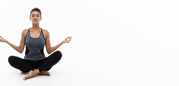 Concepto de salud y fitness Hermosa dama africana americana en ropa de fitness haciendo yoga y meditación Aislada sobre fondo blanco