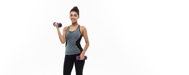 Concepto de salud y fitness Longitud total de retrato Hermosa dama africana americana en ropa de fitness gris entrenamiento con mancuernas Aislado sobre fondo blanco