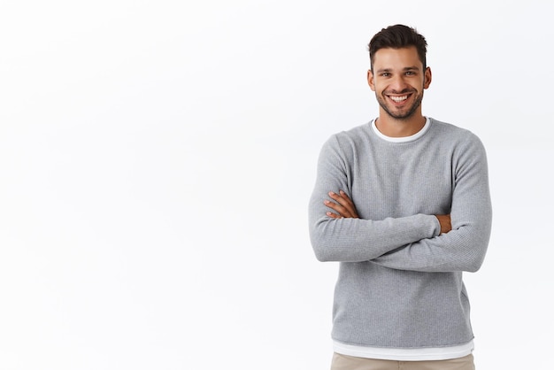 Concepto de salud de personas y hombres de felicidad Atractivo chico caucásico sonriente con barba que usa suéter gris con los brazos cruzados en el pecho en pose informal riendo y mirando la cámara charlando entusiasta