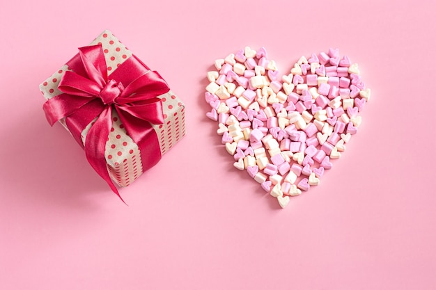 El concepto de San Valentín. Caja de regalo con lazo rojo en pared rosa.