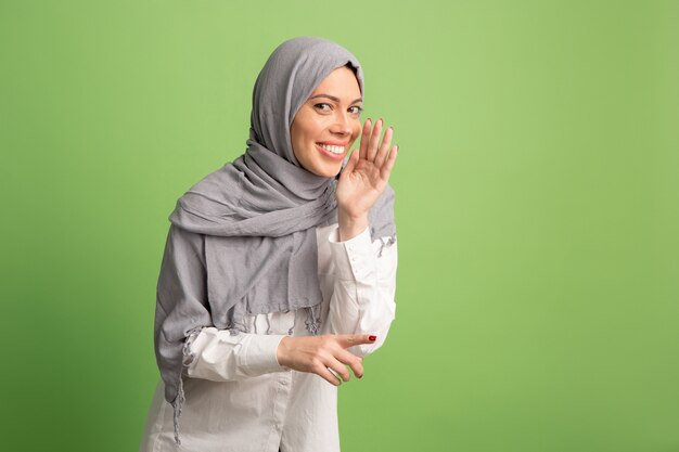 Concepto secreto de chismes. Feliz mujer árabe en hijab. Retrato de niña sonriente, posando en el fondo verde del estudio.