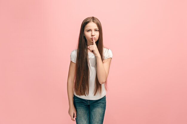 Concepto secreto de chismes. Joven adolescente susurrando un secreto detrás de su mano aislado sobre fondo de estudio rosa de moda.