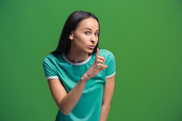 Concepto secreto de chismes. Mujer joven susurrando un secreto detrás de su mano. Mujer de negocios aislada sobre fondo de moda estudio verde. Joven mujer emocional. Las emociones humanas, el concepto de expresión facial.