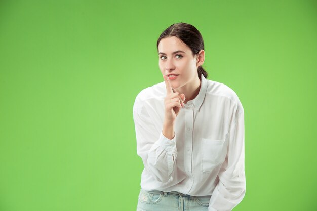 Concepto secreto de chismes. Mujer joven susurrando un secreto detrás de su mano. Mujer de negocios aislada sobre fondo de moda estudio verde. Joven mujer emocional. Las emociones humanas, el concepto de expresión facial.