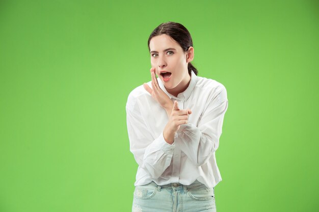 Concepto secreto de chismes. Mujer joven susurrando un secreto detrás de su mano. Mujer de negocios aislada sobre fondo de moda estudio verde. Joven mujer emocional. Las emociones humanas, el concepto de expresión facial.