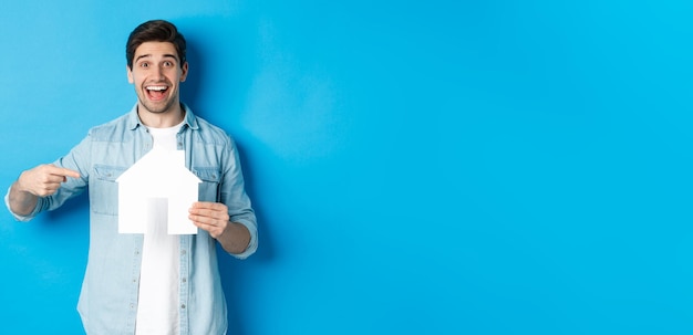 Foto gratuita el concepto de seguro hipotecario e inmobiliario sorprendió al hombre señalando el modelo de casa y la búsqueda sonriente