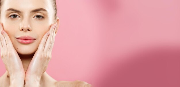 Concepto de spa de belleza Mujer caucásica con la piel de la cara perfecta Retrato Hermosa chica morena Spa que muestra el espacio de copia vacío Aislado sobre fondo de estudio rosa Proponer un producto