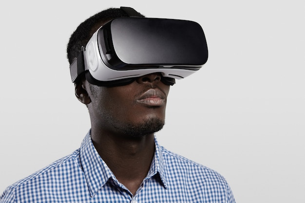 Concepto de tecnología, entretenimiento, juegos, ciberespacio y personas. Jugador serio de piel oscura con camisa a cuadros y grandes gafas 3D modernas.