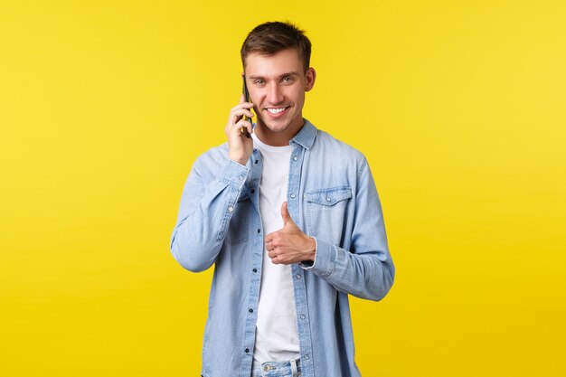 Concepto de tecnología, estilo de vida y publicidad. Hombre guapo y complacido hablando por teléfono, asegúrese de que todo vaya bien, mostrando el pulgar hacia arriba para alentarlo a que esté bien, haciendo un acuerdo mientras llama