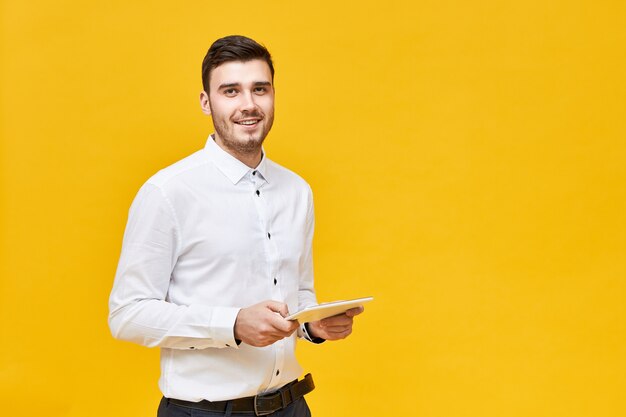 Concepto de tecnología moderna y dispositivos electrónicos. Gerente masculino joven positivo elegante con tableta digital para el trabajo. Hombre de negocios, en, ropa formal, tenencia, panel táctil, computadora portátil