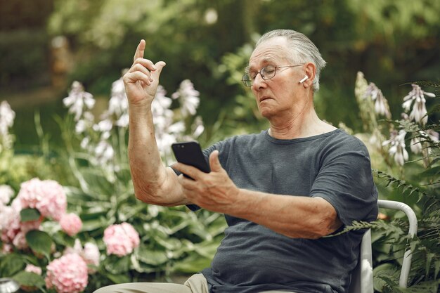 Concepto de tecnología, personas y comunicación. Hombre mayor en el parque de verano. Grangfather usando un teléfono.