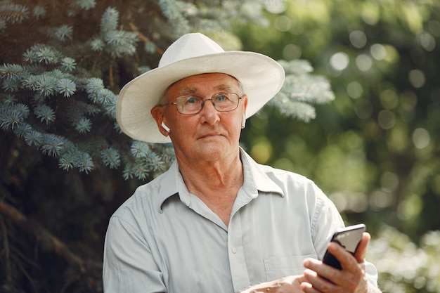 Concepto de tecnología, personas y comunicación. Hombre mayor en el parque de verano. Grangfather usando un teléfono.