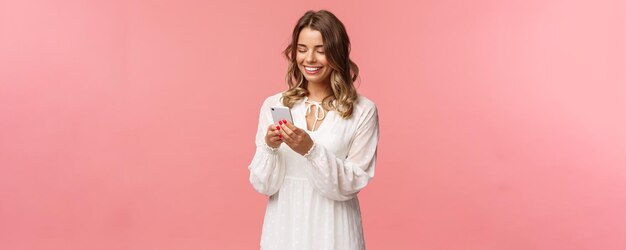 Concepto de tecnología y teléfonos inteligentes Atractiva mujer joven con un lindo vestido blanco que envía mensajes organiza citas románticas para reservar boletos a través de una aplicación en línea en el teléfono móvil sonriendo en la pantalla