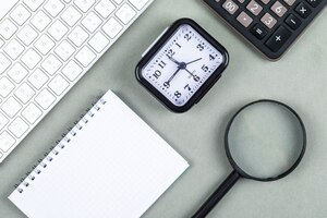 Foto gratis concepto de tiempo y dinero con teclado, calculadora, lupa, cuaderno, reloj en vista superior de fondo verde azul marino. imagen horizontal