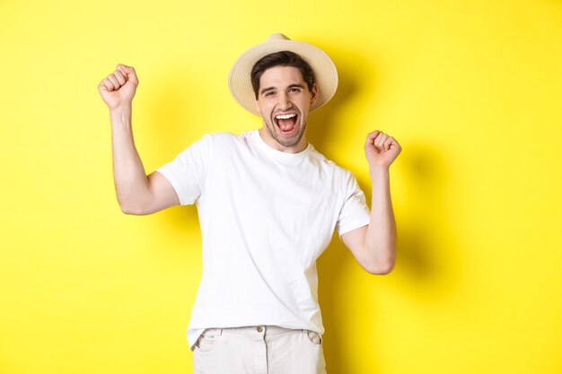 Concepto de turismo y estilo de vida. Turista de hombre feliz celebrando, regocijándose por las vacaciones, de pie sobre fondo amarillo.