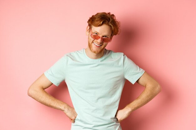 Concepto de turismo y vacaciones gracioso hombre barbudo con pelo rojo con gafas sonriendo y mirando a otro lado ...