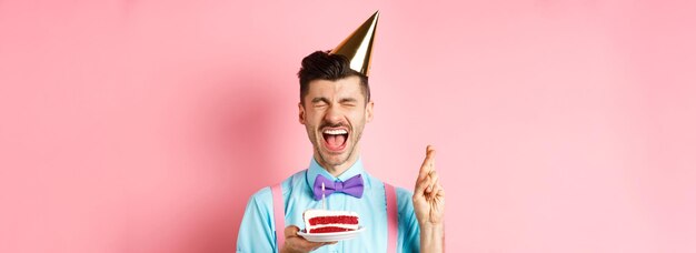 Foto gratuita concepto de vacaciones y celebración emocionado chico celebrando cumpleaños y deseando cruzar los dedos para