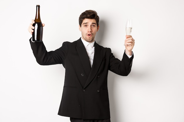 Concepto de vacaciones, fiesta y celebración. Imagen de hombre guapo en traje elegante, bailando con una botella de champán, bebiendo en año nuevo, de pie sobre fondo blanco.