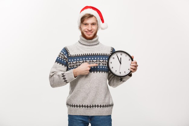 Concepto de vacaciones Hombre joven y guapo con barba que señala el reloj blanco que dice la hora