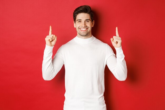 Concepto de vacaciones de invierno apuesto joven con cerdas vistiendo suéter blanco mostrando christma ...