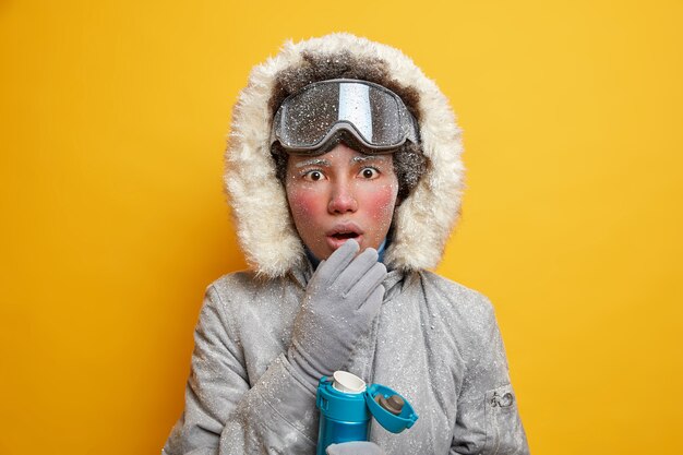 Concepto de vacaciones de invierno. La mujer activa étnica sorprendida disfruta de la actividad deportiva y mantiene la boca abierta debido a las bebidas calientes vestidas con ropa de abrigo.