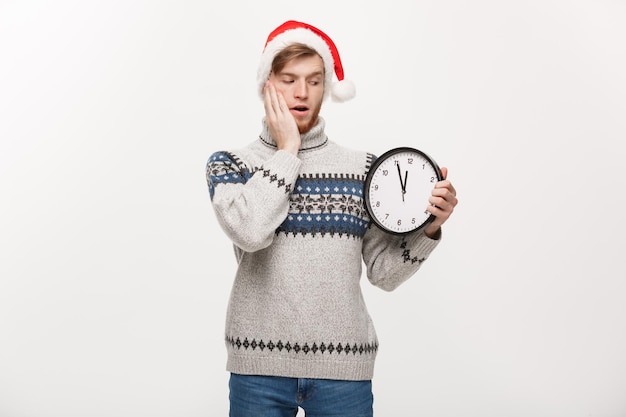 Concepto de vacaciones Joven hombre de barba guapo feliz en suéter sosteniendo reloj blanco sobre fondo blanco de estudio