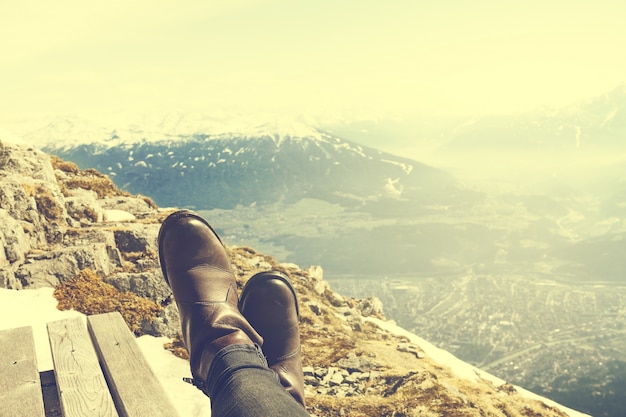 Concepto De Las Vacaciones Del Viaje. Pies de las piernas de Chica Joven escalofriante en banco de madera sobre fondo de montaña de la naturaleza. Horizontal. Viraje.