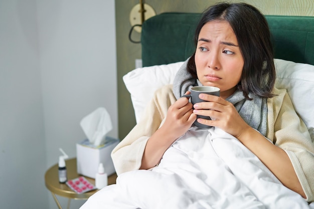 Foto gratuita concepto de vacunación y gripe covid niña coreana acostada en la cama con gripe que se resfría bebiendo agua caliente