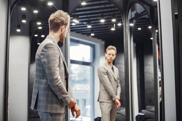 Concepto de venta, compras, moda, estilo y personas. Hombre joven elegante eligiendo ropa en centro comercial o tienda de ropa.