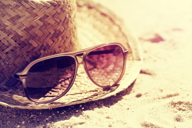 Concepto Del Verano O De Las Vacaciones. Gafas de sol hermosas con el sombrero de paja en la arena. Playa. Estilo de vida. Viraje.
