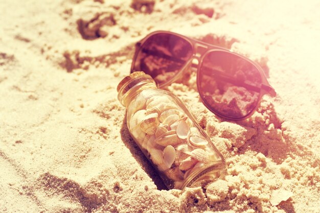 Concepto del verano o de las vacaciones. Seashells en botellas en la arena. Viraje.