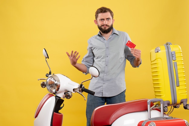 Concepto de viaje con ambicioso joven parado detrás de la motocicleta y sosteniendo una tarjeta bancaria en amarillo