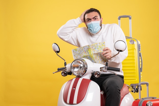 Concepto de viaje con chico confundido en máscara médica sentado en motocicleta con maleta amarilla en él