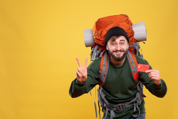 Concepto de viaje con chico joven sonriente con packpack y sosteniendo una tarjeta bancaria mostrando dos en amarillo