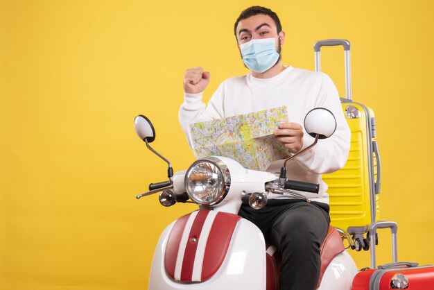 Concepto de viaje con chico orgulloso en máscara médica sentado en motocicleta con maleta amarilla y sosteniendo mapa en amarillo