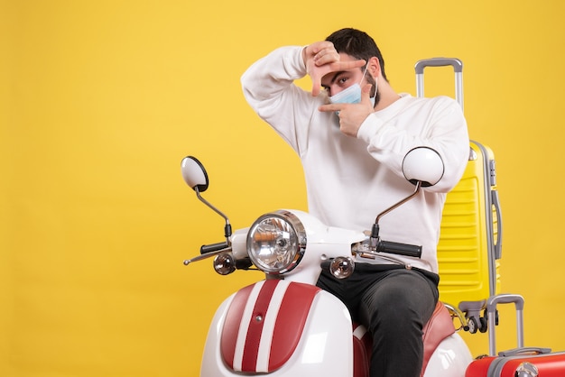 Concepto de viaje con chico seguro en máscara médica sentado en motocicleta con maleta amarilla en amarillo