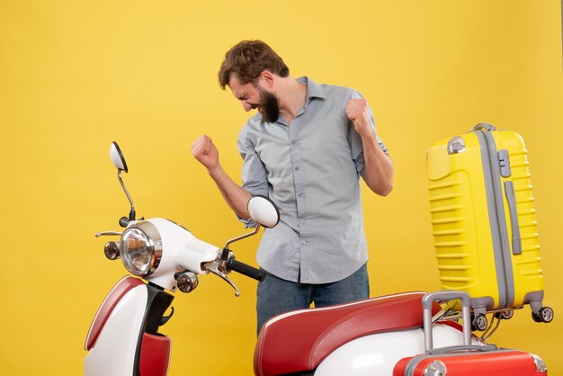 Concepto de viaje con feliz emocional joven parado detrás de la motocicleta con maletas sosteniendo el boleto en amarillo