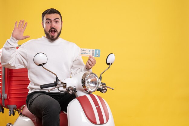 Concepto de viaje con hombre emocional sentado en motocicleta con maleta mostrando boleto en amarillo