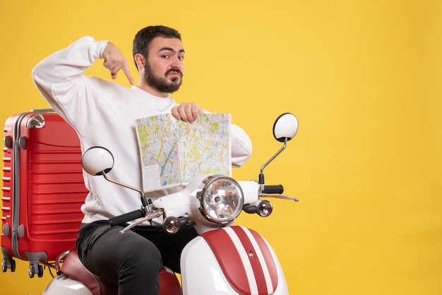 Concepto de viaje con hombre sorprendido sentado en motocicleta con maleta apuntando mapa en amarillo