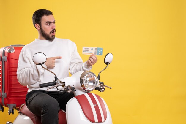 Concepto de viaje con hombre sorprendido sentado en motocicleta con maleta mostrando billete en amarillo