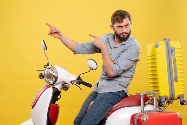 Concepto de viaje con joven barbudo emocional sentado en motocicleta apuntando hacia arriba en amarillo