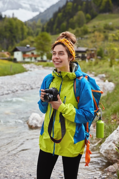 Concepto de viajes y actividades al aire libre. Caminante femenino encantador optimista camina por el pequeño arroyo de montaña