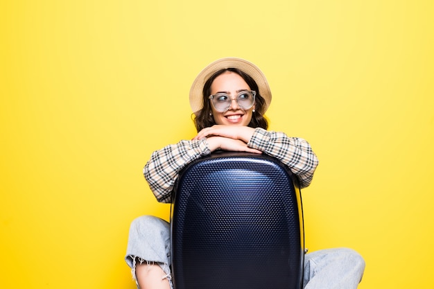 Concepto de viajes y estilo de vida. Retrato de una niña con sombrero de paja y gafas de sol con maleta mirando aislado