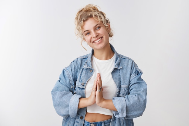 Concepto de yoga de bienestar namaste. Tierna mujer rubia de pelo rizado ojos azules inclinar la cabeza presionar palmas orar gesto sentirse aliviado, relajado terminar meditando pacíficamente de pie pared blanca