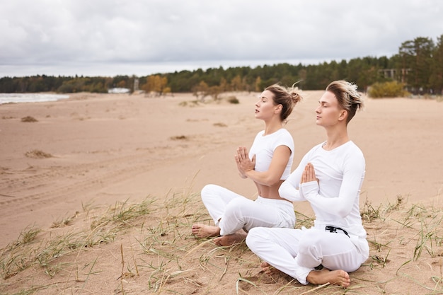 Concepto de yoga, zen, iluminación, recreación, meditación y concentración. Hombres y mujeres jóvenes con ropa blanca meditando con los ojos cerrados, haciendo el gesto de namaste, sentado en la postura del loto