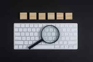 Foto gratuita conceptual de investigación con teclado, lupa, cubos de madera sobre fondo negro escritorio plano lay. imagen horizontal