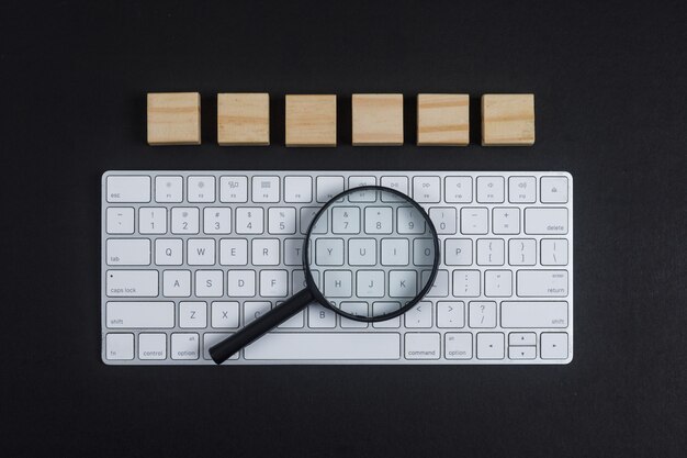 Conceptual de investigación con teclado, lupa, cubos de madera sobre fondo negro escritorio plano lay. imagen horizontal