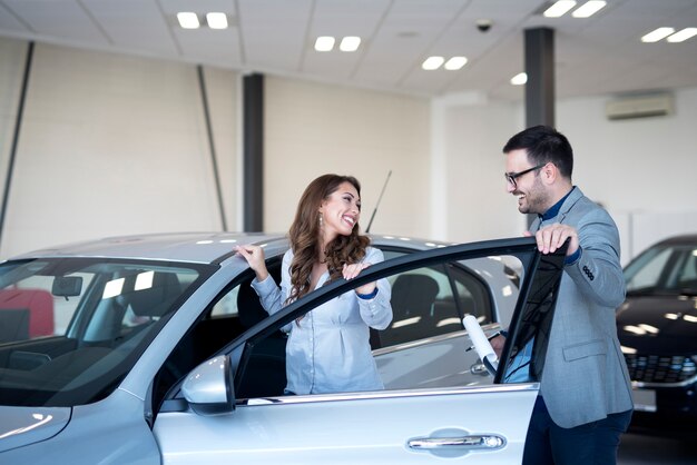 Concesionario de coches y cliente en la sala de exposición de vehículos eligiendo coche nuevo