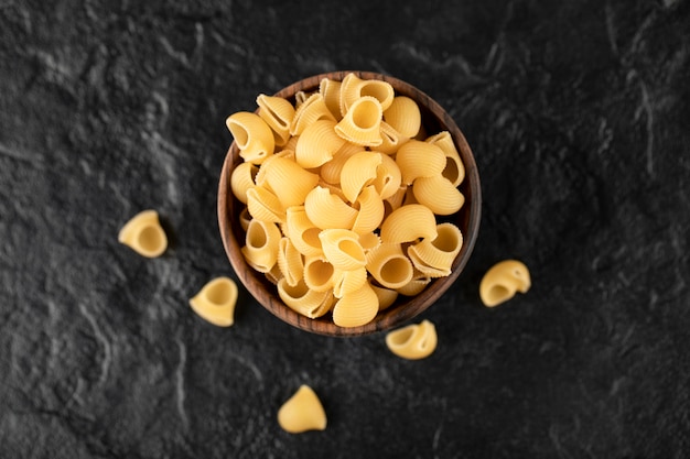 Conchiglie de pasta cruda italiana en cuenco de madera.