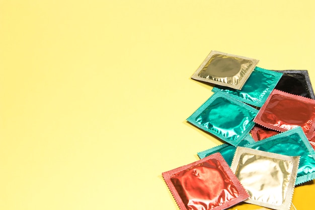 Condones coloridos de alto ángulo sobre fondo amarillo